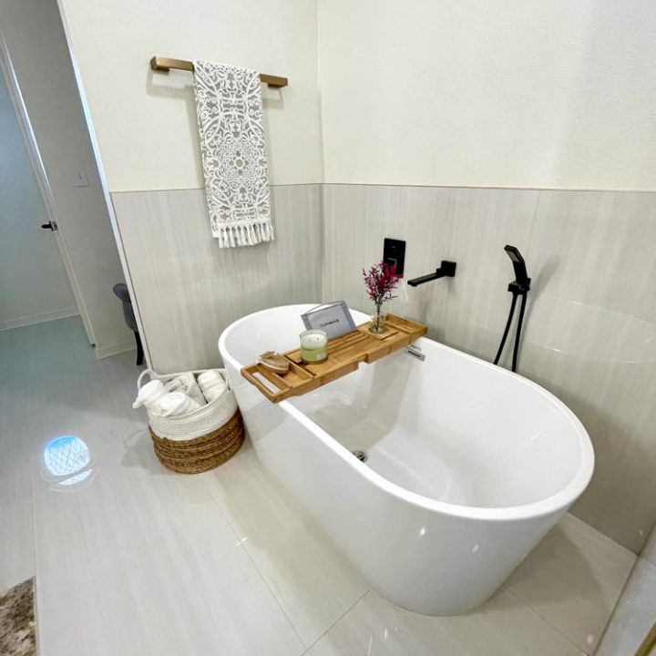 a single bathtub with a black telephone shower, a towel basket on the floor, and a hanging towel